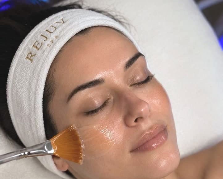 A guest resting in a Rejuv headband while a treatment serum is brushed onto her cheek