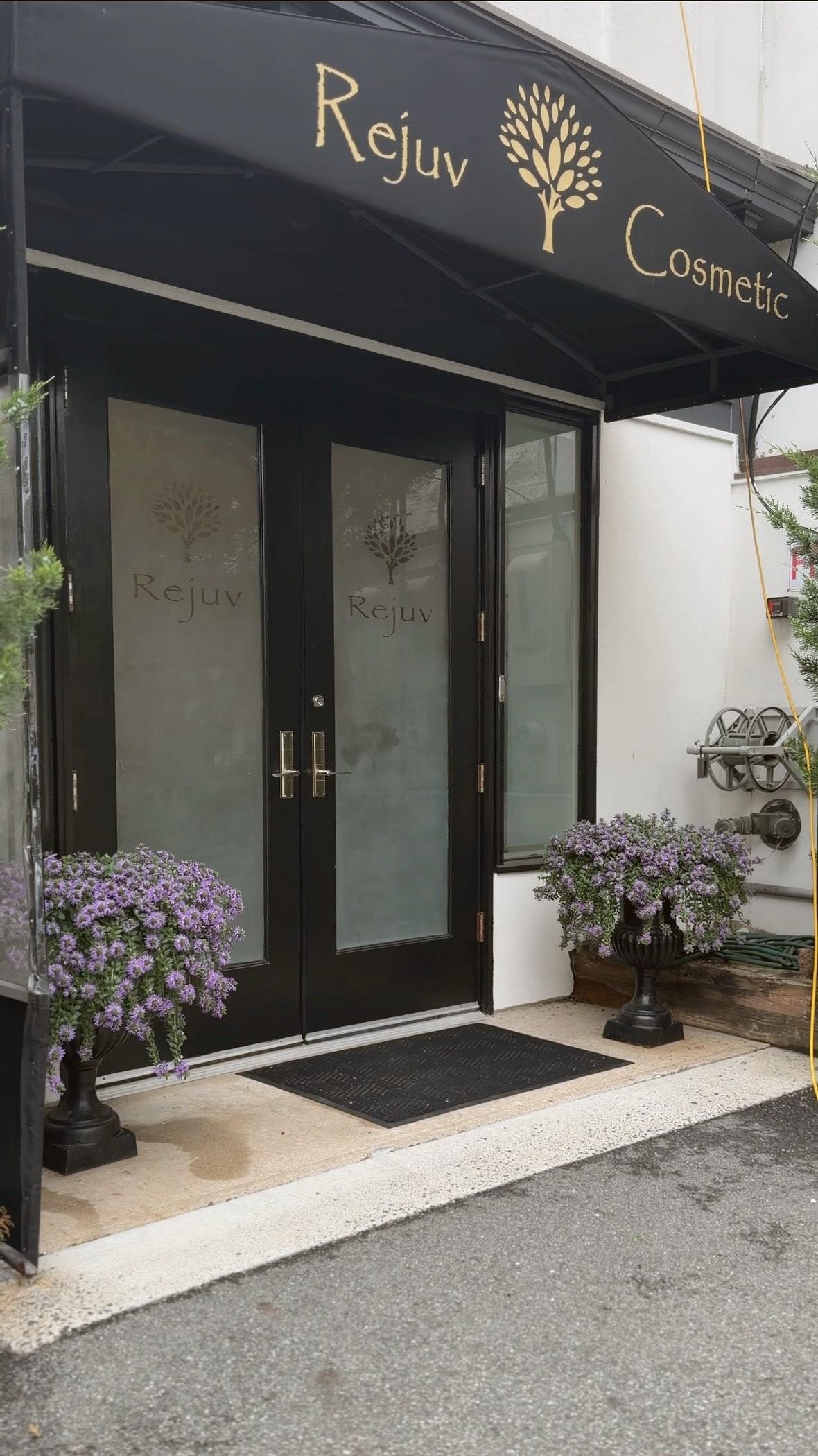 The entrance to Rejuv Cosmetic Center & Spa — a dark awning over glass doors etched with the Rejuv mark, flanked by urns of lavender